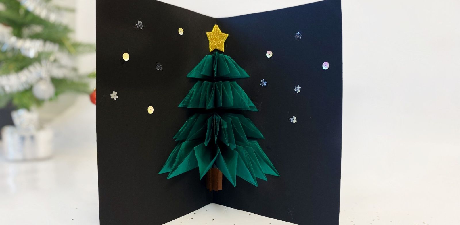 Handgjort pop-up-julkort med origamigran och stjärndekor mot svart bakgrund